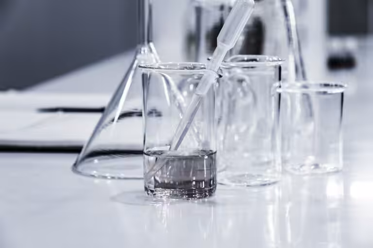 Tre becher di vetro trasparenti su un banco di laboratorio, usati per le analisi di caratterizzazione dei rifiuti
