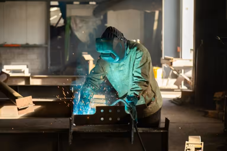 Operaio saldatore con casco protettivo e torcia che salda profili metallici in officina, investimenti in sicurezza nelle PMI